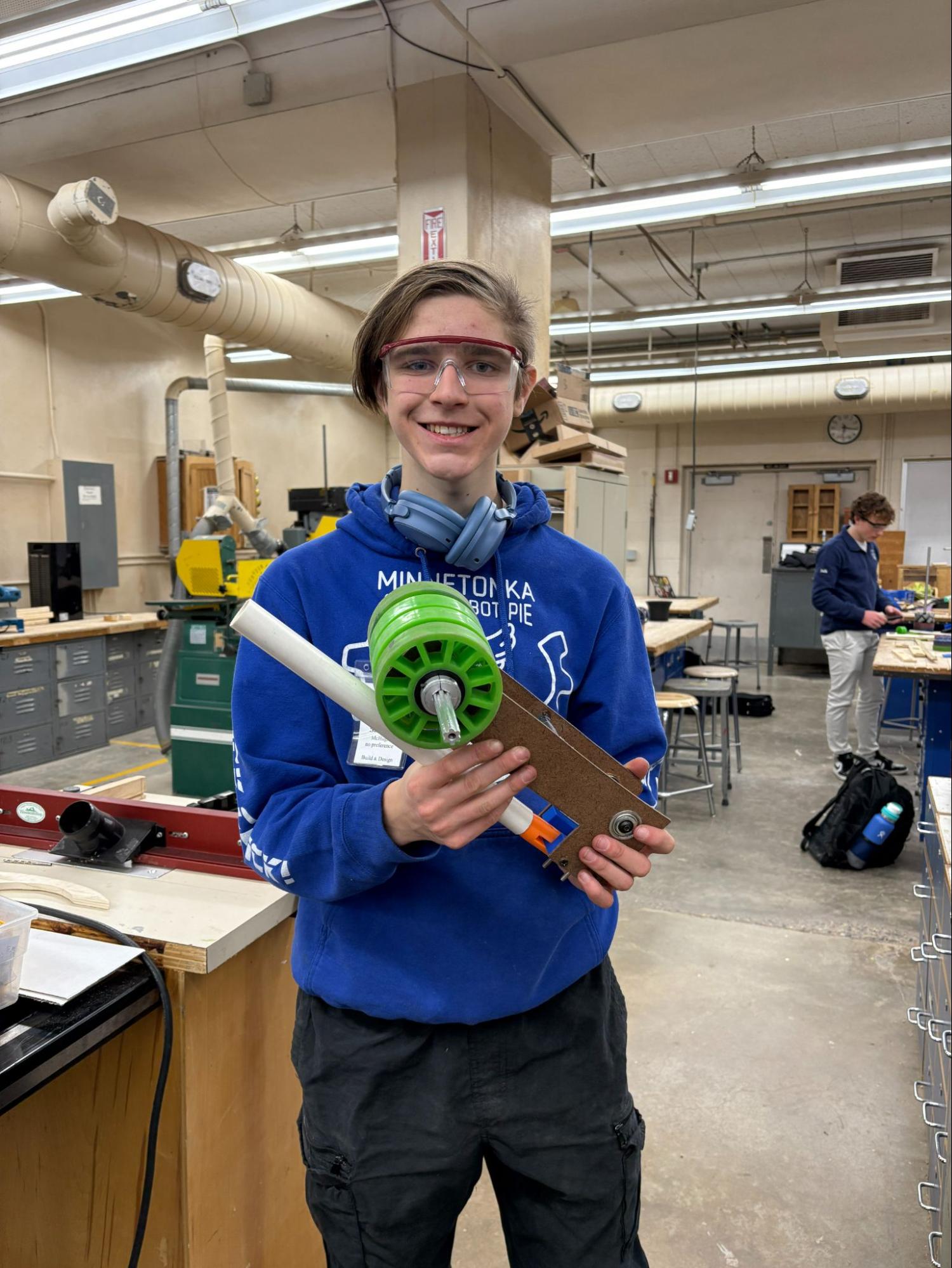 Sam is pictured holding a PVC pipe with two green wheels above it attached by a piece of wood at the end of the pipe