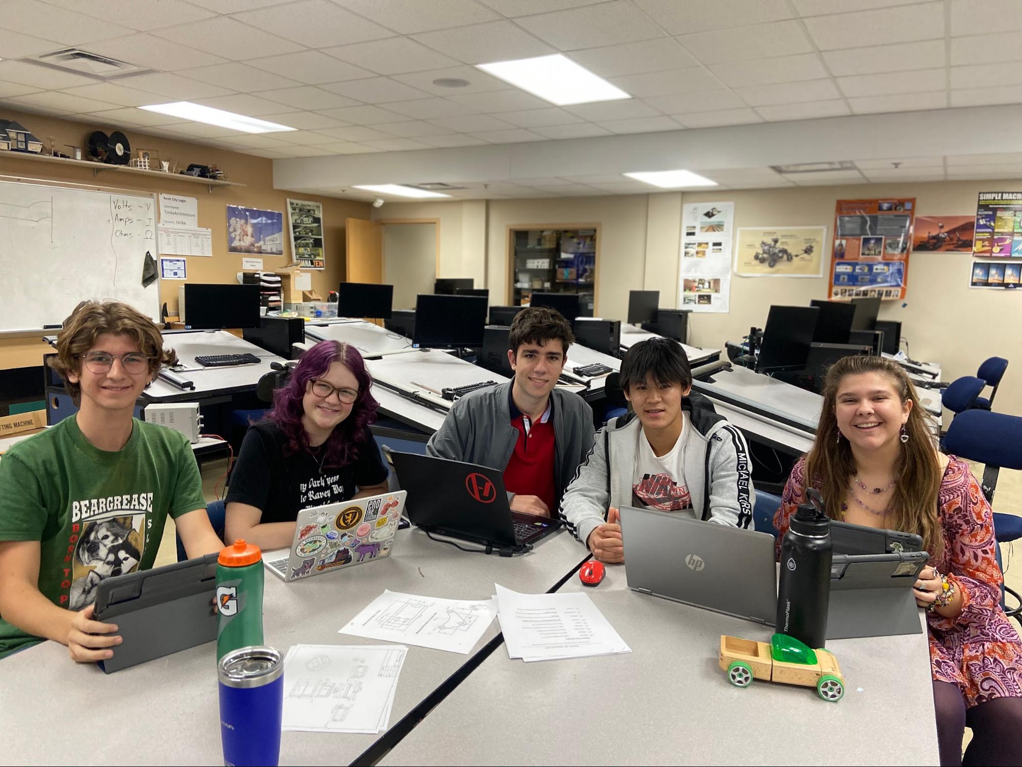 Operations team working in the CAD room with their devices on the table in front of them. They are smiling and look excited to be there.