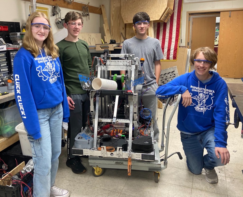 3 programming members and the safety captain posing around last year robot, smiling.