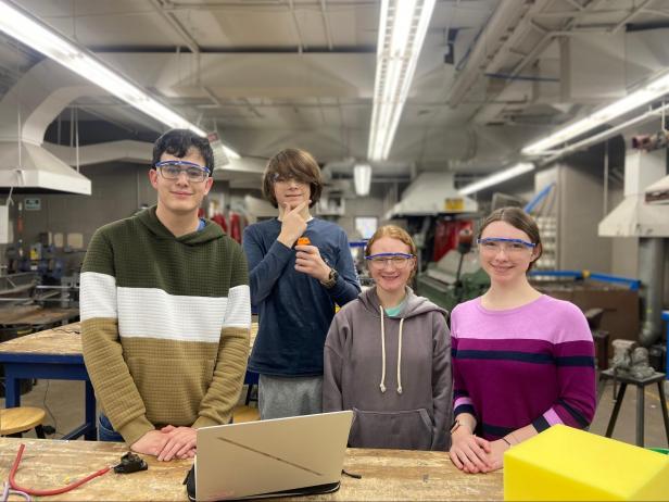 4 members of the programming team in the metal shop smiling for the camera. 